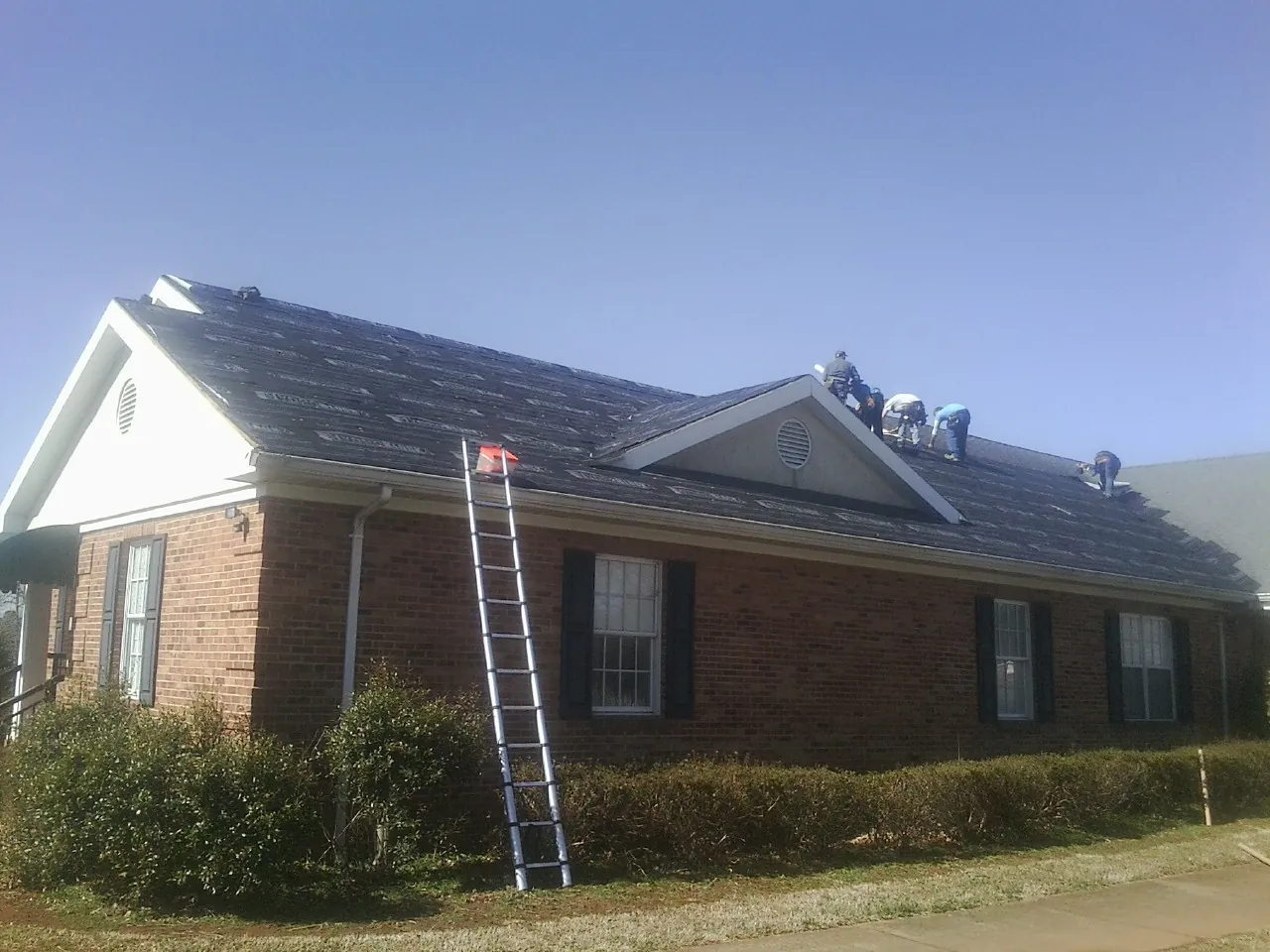Crew tearing shingles off a brick ranch roof with a ladder set — Emergency Roof Repair work by our crew in Carmel