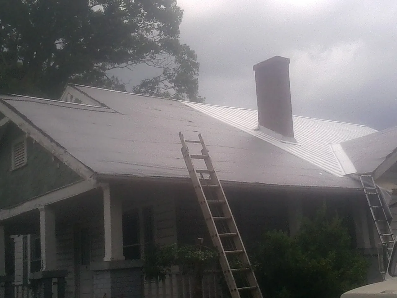 Ladders against a metal roof on an older home with a brick chimney in Carmel