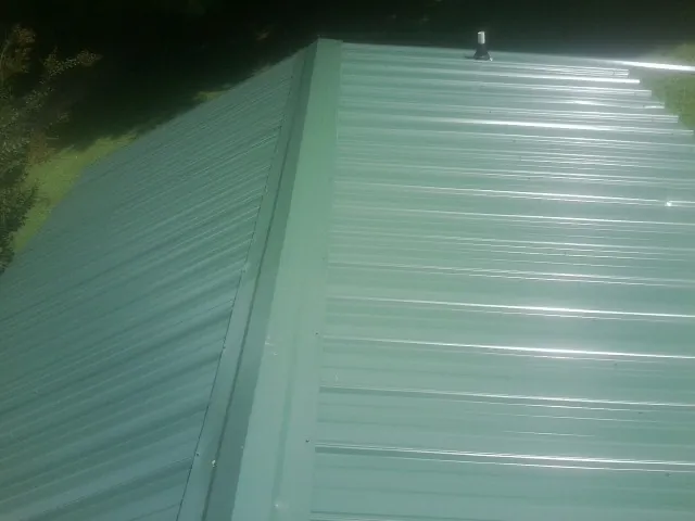 New green metal panels meeting at the ridge of a roof — Flat Roof Repair work by our crew in Carmel