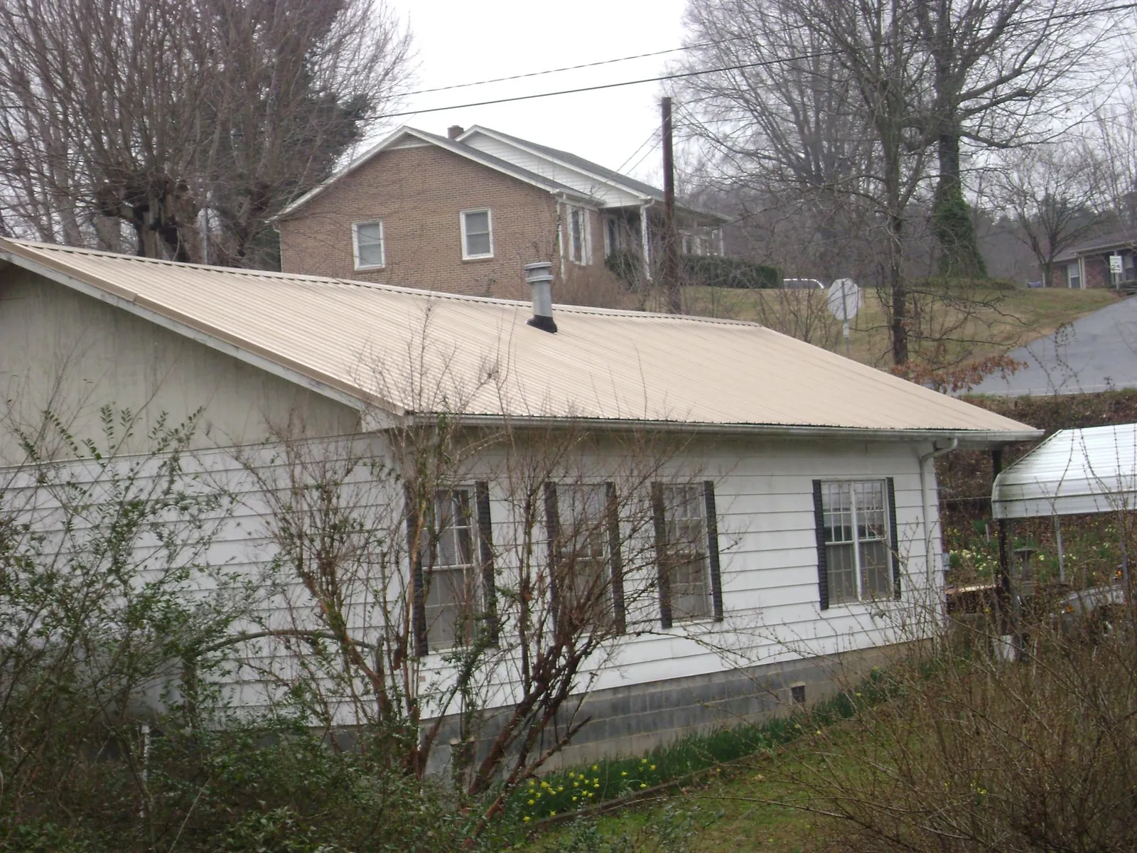 Tan metal roof on a white sided house set into a hillside — Commercial Roofing by Roofing Brothers in Carmel